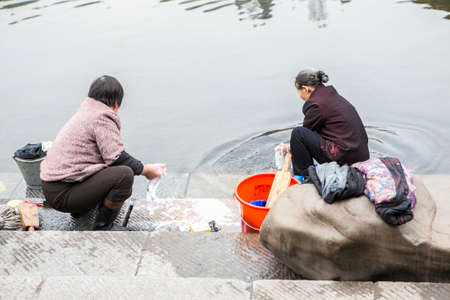 FengHuang, China Feb 21, 2014 : two asian women are washing and cleaning their clothes at step stair next to the river by using hand as a history of the traditional washingのeditorial素材