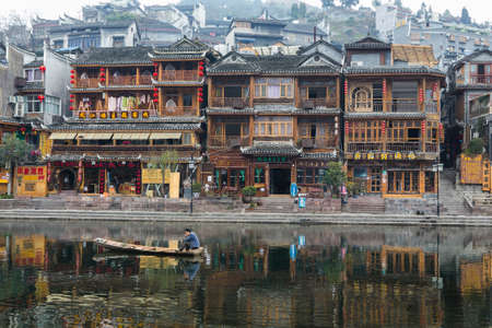 FengHuang, China Feb 21, 2014 : traditional chinese houses in Fenghuang village with chinese character signs and asian man in a boat on riverのeditorial素材