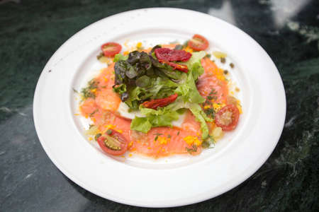 smoked salmon salad and sundried tomatoes with italian dressing sauce served in a plain white round plate on black marble table backgroundの写真素材