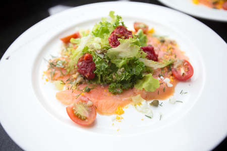 close up smoked salmon salad and tomatoes sundried with italian dressing sauce decorated with parsley dill on white round plateの写真素材