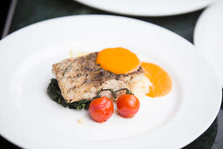 close up of grilled seabass fish fillet served with orange sauce decorated with tomato and spinach...