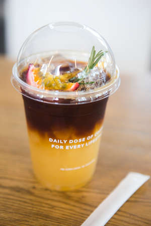 SamutPrakan,Thailand - July 8, 2020 a plastic glass with a cover lid of ice americano coffee drink blend with passion fruit ginger ale and brown sugar separate in two color layers with tube besideのeditorial素材
