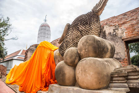 closeup at the back of a big sleeping buddha statue cover by orange cloth in an ancient ruins outdoor chapel which making from red brickの写真素材