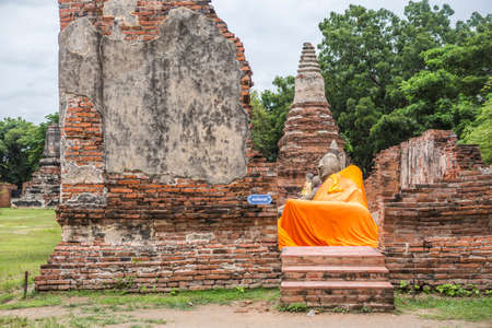 Thai word in blue sign written mean 'saiyayan buddha' a big sleeping buddha statue cover by orange clothe in an ancient ruins chapel which making from red brickの写真素材