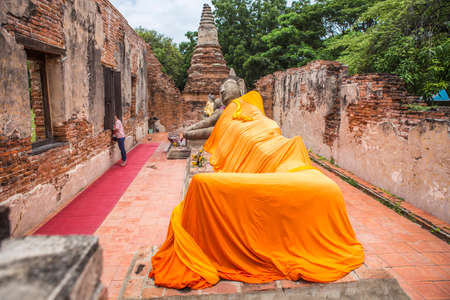 a big sleeping buddha statue cover by orange cloth in an ancient ruins chapel which making from red brickの写真素材