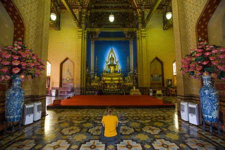 Bangkok, Thailand - 30 August 2020: a female is sitting in a middle of classic thai traditional style chapel in front of golden big buddha statueのeditorial素材