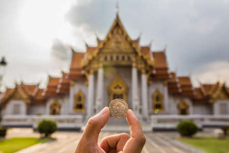 Bangkok, Thailand - 30 August 2020: hand holding thai 5 baht coin with blur traditional classical thai temple as a backgroundのeditorial素材
