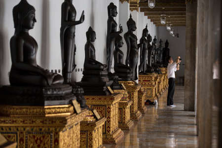 Bangkok, Thailand - 30 August 2020: an asian male is taking photo while black buddhist sculptures are arranging behind himのeditorial素材
