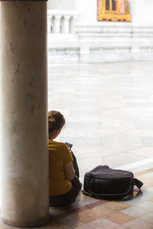 Bangkok, Thailand - 30 August 2020: a female with yellow t-shirt is sitting on marble floor in thai...