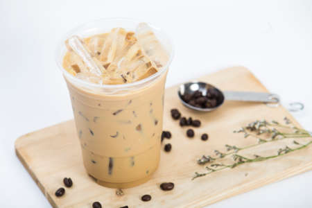 blur of cool iced coffee with milk in a plastic glass 16oz. put on small wooden cutting board with coffee beans in a teaspoon and flower decoratedの写真素材
