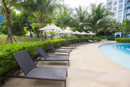 Prachuap Khiri Khan, Thailand-November 10, 2020: outdoor rattan beach lounge chairs are arranging around swimming pool of condominium which surrounding by green treesのeditorial素材