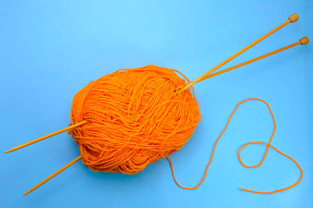 knitting orange yarn with knitting needles on a blue background