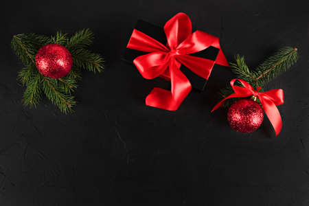 christmas card fir branches with red ornament balls and black gift with red ribbon on black backgroundの写真素材