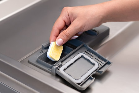 female hand puts dishwasher tablet into open automatic built-in dishwasher machine. Close up.の写真素材