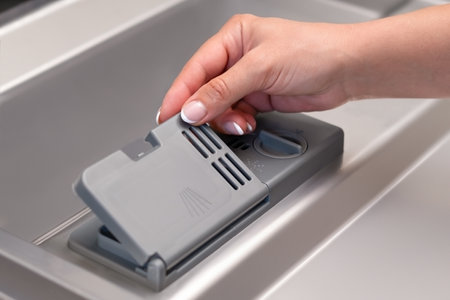 female hand puts dishwasher tablet into open automatic built-in dishwasher machine. Close up.の写真素材