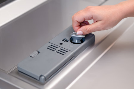 female hand puts dishwasher tablet into open automatic built-in dishwasher machine. Close up.の写真素材