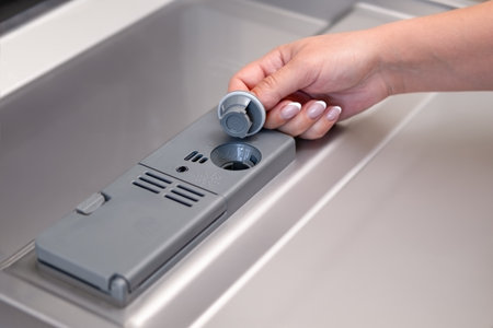 female hand puts dishwasher tablet into open automatic built-in dishwasher machine. Close up.の写真素材
