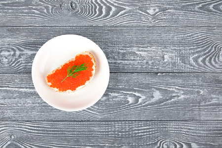 Sandwich with butter and red caviar on a white plate and gray wooden table.の写真素材