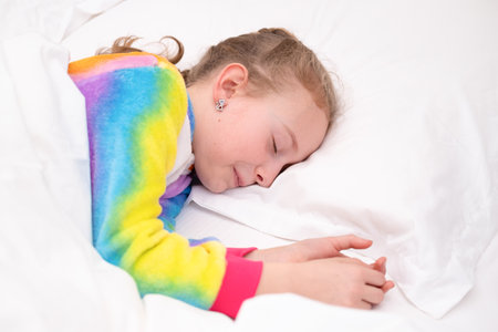 Little girl sleeping in bright colorful pajamas on a white pastel background close up.