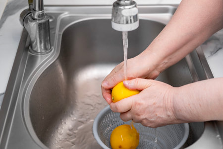 Women's hands wash a lemon in a sink under running water from a tap.の写真素材