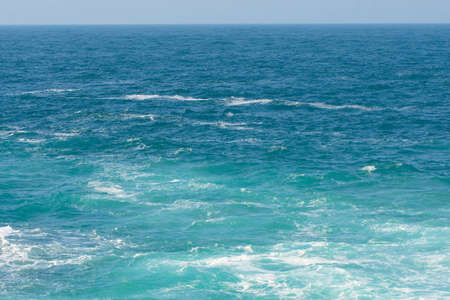 blue sky and sea with some white foam wavesの写真素材