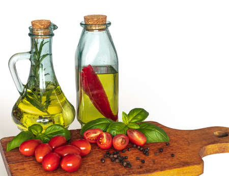 Bottles with salad oil. Taste of rosemary, garlic and peppers. Tomatoes with basil. Italian cuisine. White background, a cutting board.の写真素材
