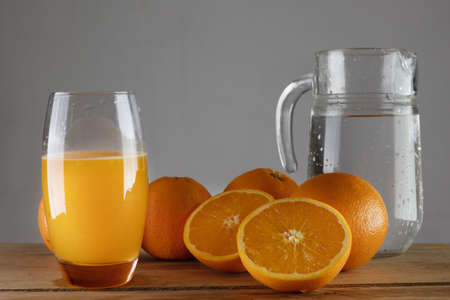 Oranges on a wooden table. A jug of water and a glass of juice. Fresh, squeezed orange juice.の写真素材