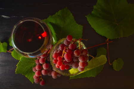 Grapes in the cup. Green vine leaves. Black background. Time for red wine. Still life. A glass of red wine.の写真素材