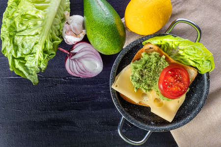Toast with avocado, cheese and tomato. Breakfast sandwich. Preparation of a healthy breakfast. Lettuce, onions, garlic and avocado. Breakfast time.の写真素材