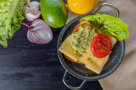 Toast with avocado, cheese and tomato. Breakfast sandwich. Preparation of a healthy breakfast. Lettuce, onions, garlic and avocado. Breakfast time.の写真素材