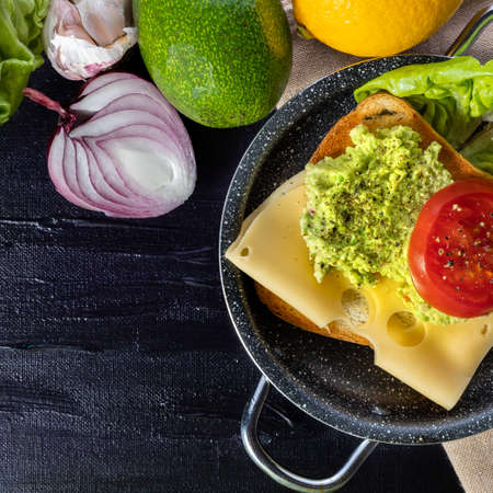 Toast with avocado, cheese and tomato. Breakfast sandwich. Preparation of a healthy breakfast. Lettuce, onions, garlic and avocado. Breakfast time.の写真素材