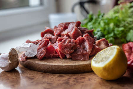 Beef meat for goulash. Raw red meat on wooden board. Lemon, red pepper and garlic.