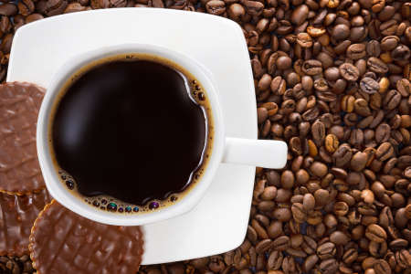 White cup of hot coffee on a background of brown beans. Three chocolate biscuits.の写真素材