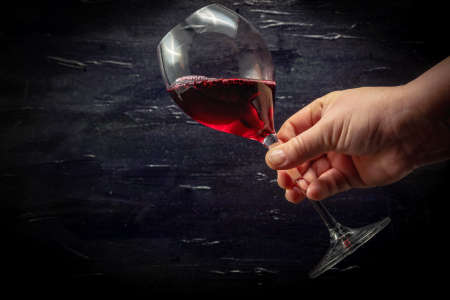A hand holding a glass of red wine. Black background.の写真素材