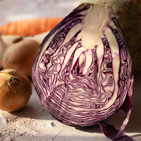 Half a red cabbage on a rustic table. In the background onion, parsley root and carrots. Vegetables for salad or soup. Vegan diet. Healthy food.の写真素材