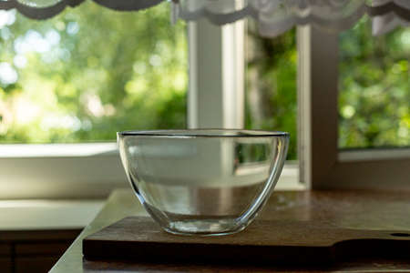 Glass bowl on a wooden board. Rustic table with a window to the garden in the background.の写真素材