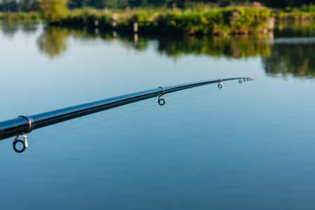 Fishing rod on the background of water. Fishing on a pond, lake. Depth of field. Relax in the morning. Holiday sports. Summer in Poland.の写真素材