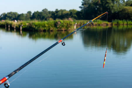 A float on a fishing rod in the background of a pond. Recreation in the morning. Fishing on the lake. Water Sports. The landscape of Mazovia. Vacations in Poland. Summer entertainment.の写真素材