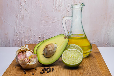 Avocado paste products. Avocado, lime, garlic, pepper on a wooden board. Olive oil in a glass transparent bottle. Bright rustic background. Italian cuisine. Restaurant equipment.の写真素材