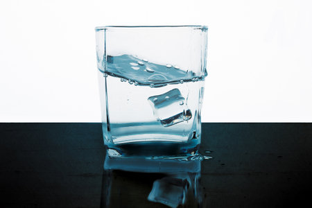 Glass of water with ice cubes on a black table, isolated on white backgroundの写真素材