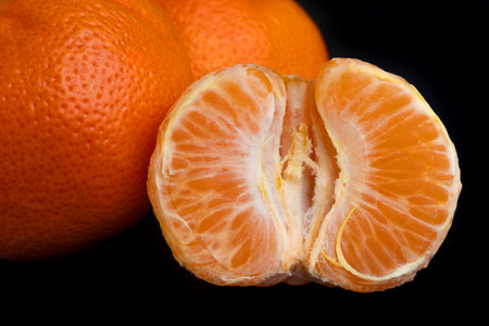 Half of a peeled tangerine against the background of other whole tangerines. The photo background is black. Healthy food. Juicy fruits. Citrus in the kitchen.の写真素材