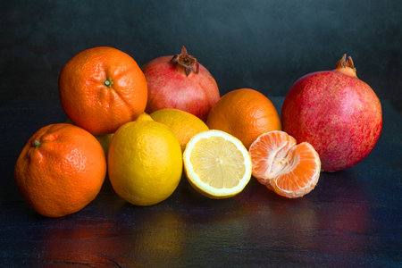 Tangerines, lemon, and pomegranate on a dark, graphite, black background. Healthy fruits. Health in the kitchen. Tropical fruits.の写真素材