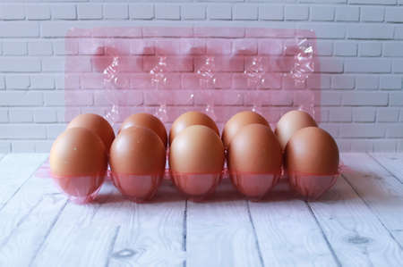 Photo of ten eggs in a pink plastic packing rack on a wooden tableの写真素材