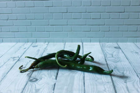 Photo of a pile of long green chilies on a wooden tableの写真素材