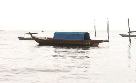 Photo of a dark brown boat with a blue roof being moored on the shoreの写真素材