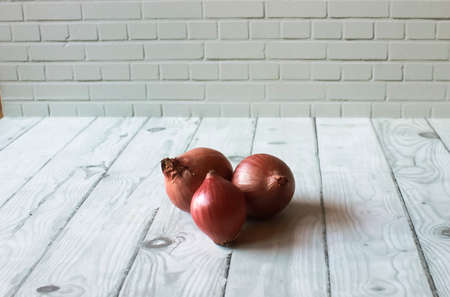 Photo of three red onions on a wooden patterned table against a stone wall backgroundの写真素材