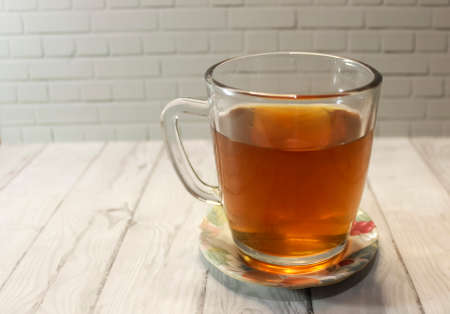 Photo of tea in a clear glass cup on a wooden table and stone wall backgroundの写真素材