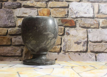 Photo of an antique cup made of natural stone in black on a rock pile wall backgroundの写真素材