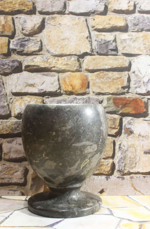 Photo of an antique cup made of natural stone in black on a rock pile wall backgroundの写真素材