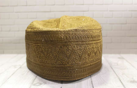 A photo of a Moslem prayer cap on a wooden patterned table with a stone wall as a backgroundの写真素材